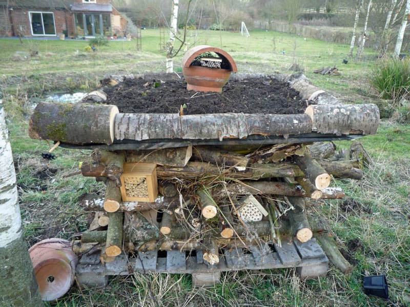 Wooden wildlife habitat stack with logs, soil and insect houses in a garden
